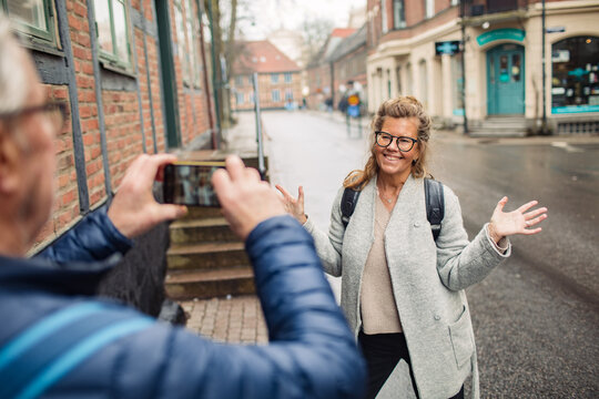 Smiling mature woman posing for smartphone photo on rainy city street