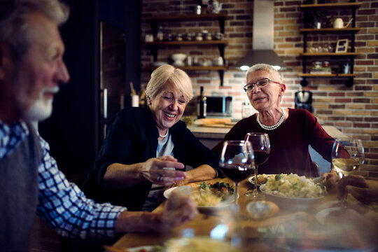 Senior friends laughing over dinner at home kitchen