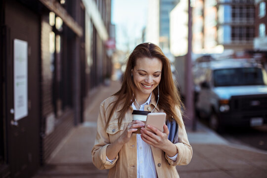 Smiling young woman with coffee using smartphone on city street