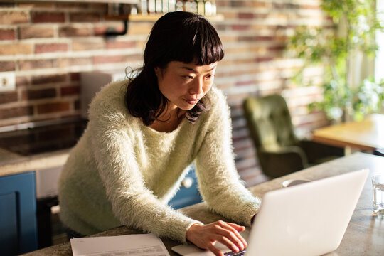 Woman working on laptop in cozy home kitchen