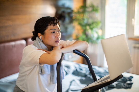 Woman on exercise bike watching online workout at home