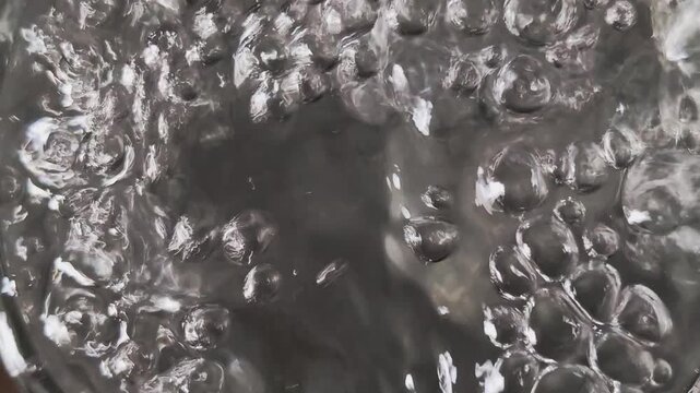 Close up view of boiling water with transparent bubbles rising to the surface and bursting, creating a dynamic and powerful abstract background of simmering liquid