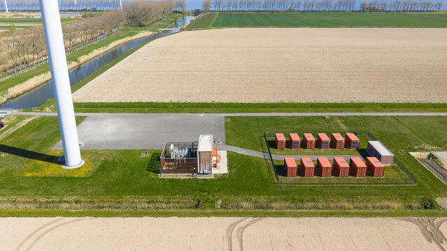 Aerial view of a wind turbine base and battery energy storage system with red containers and an electrical substation in a rural landscape Middelharnis, Zuid-Holland, Netherlands.