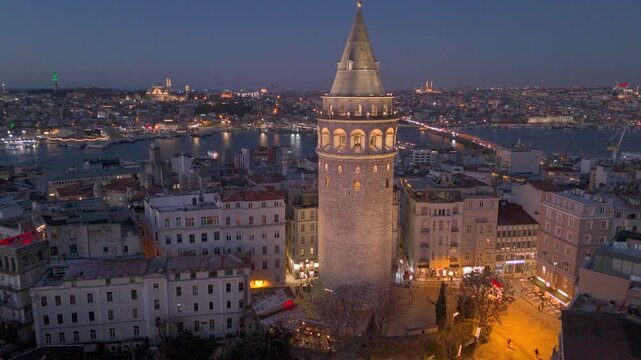 Morning view of Galata Tower illuminated against historic Golden Horn and cityscape in Istanbul with lights illuminating streets and buildings at sunrise. Flying around iconic Galata Tower in sunset.