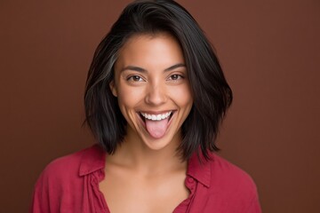 Fototapeta premium Young woman sticking out tongue in brown studio portrait