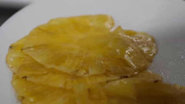 A person wearing hygienic gloves handles delicate, bright yellow dried pineapple slices, possibly preparing them for packaging or display. The focus is on the texture and vibrant color of the healthy,