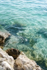Obraz premium Clear blue water meets rocky shore with sunlight reflecting on the surface near the sea in a coastal location