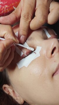 Woman undergoing an eyelash lifting and tinting process at a beauty salon, with a technician carefully applying solutions to her upper lashes for cosmetic enhancement