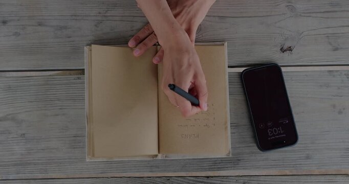 Overhead Top Down View Of Hands Using Smartphone For Calendar Planning Over Notebook On Wooden Desk, Digital Scheduling And Productivity Concept