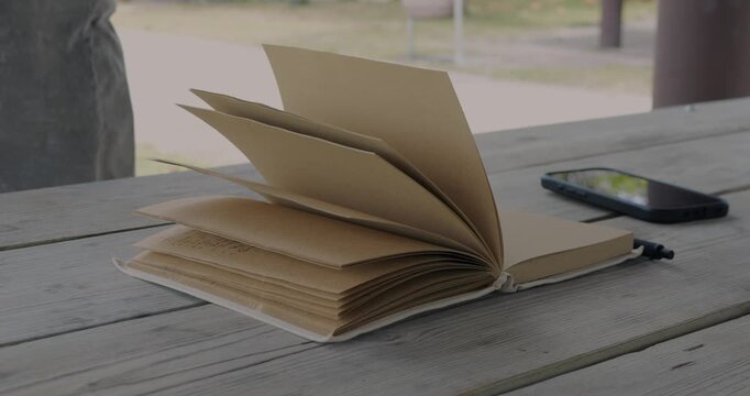 Open Notebook With Turning Pages and Smartphone on Wooden Table, Capturing a Quiet Moment of Journaling, Study, and Reflective Planning
