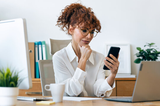 Beautiful mature business woman using smartphone while working in the office