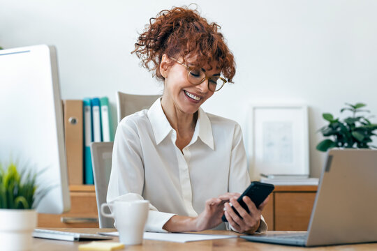 Beautiful mature business woman using smartphone while working in the office