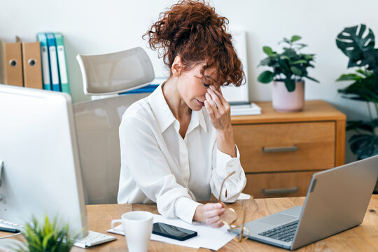 Tired mature woman with headache looking uncomfortable while working on a computer in the office