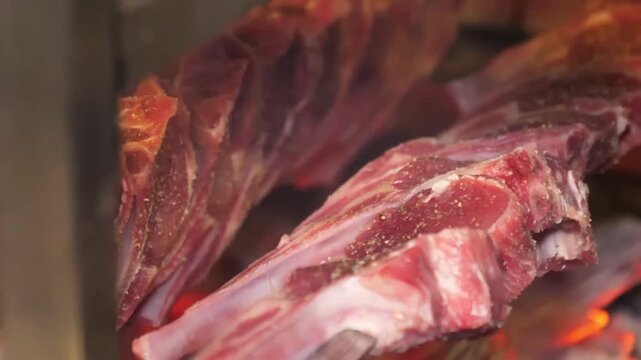 A close-up shot of fresh, seasoned mutton ribs (lamb chops) arranged on a metal skewer, prepared for traditional open-fire or charcoal barbecue. The meat shows natural marbling and texture, highlighti
