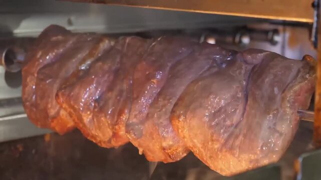 A close-up shot of seasoned Picanha steaks (rump cap) spinning on a rotisserie skewer. The meat features a thick, golden fat cap that renders and bastes the beef over the heat, creating a succulent an