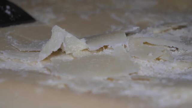 A high-quality close-up footage capturing the artisanal process of creating Raspadura. A specialized flexible blade is skillfully used to shave paper-thin, delicate veils from the surface of a young G