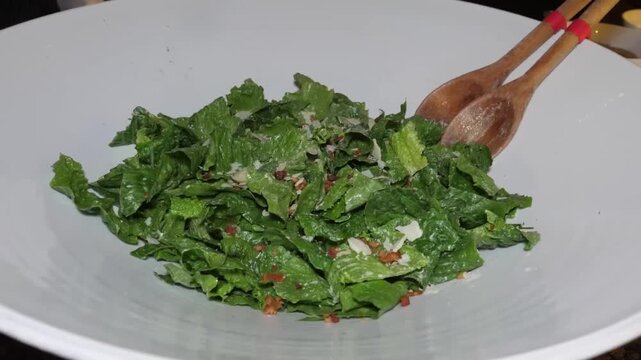 Close-up shot of a classic, old-fashioned wilted lettuce salad, also known as "kilt lettuce," in a large white serving bowl. The fresh green leaf lettuce has been tossed with a warm, sizzling bacon vi