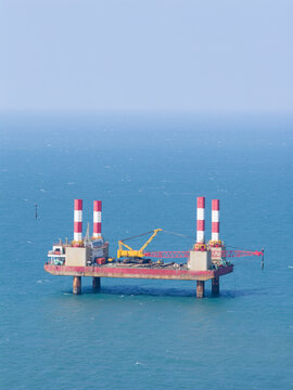 Aerial view of an offshore construction platform with red and white striped towers and a yellow crane on the blue sea in Taiwan.