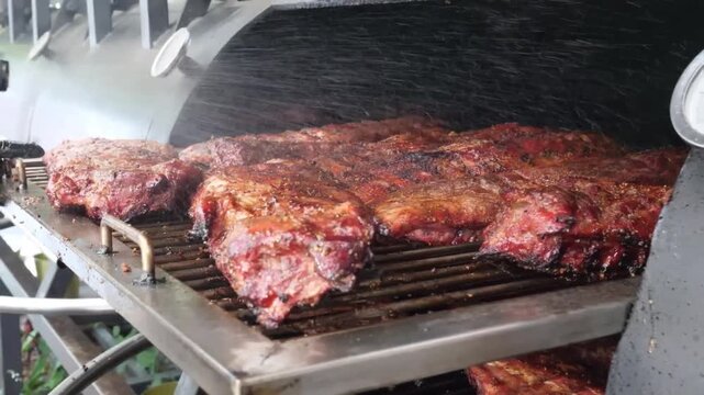 Close-up shot of multiple racks of seasoned St. Louis style ribs slow-smoking on a two-shelf commercial barbecue pit. The meat is tender, juicy, and has a rich, smoky color, ready for serving at a res