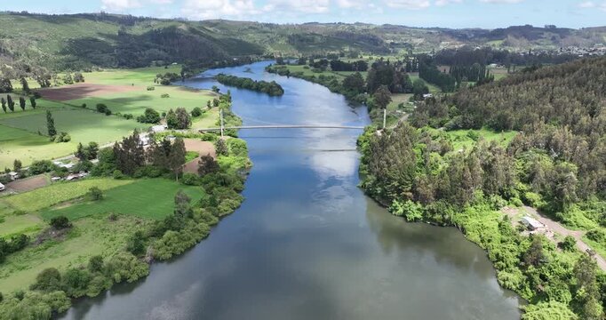 Toma con dron de Puente colgante sobre el r&iacute;o Imperial en La Araucan&iacute;a rodeado de bosque verde y d&iacute;a soleado