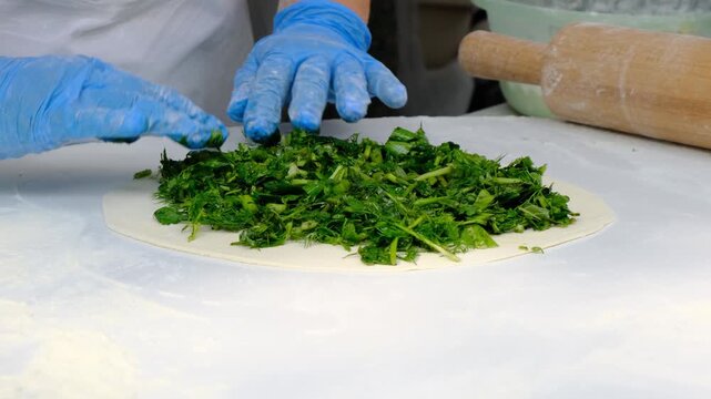 Baker cooks vegetarian flatbread with filling of many wild herbs jingyalov hats or lobiani phlovani gozleme kuku sabzi or kutaby with greens. Festival of national food of western Asia and middle east.