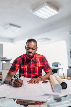 Architect reviewing blueprint and drafting notes in office