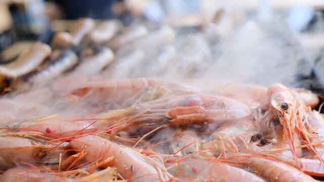 Fresh batch of royal pink juicy shrimp releases light smoke while grilling on hot open grill grate at gastronomic festival. Cooking shrimp on grill. Summer food festival. Grilled seafood.