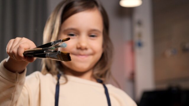Young child smiling, enthusiastically offering a handful of paintbrushes for creative artwork