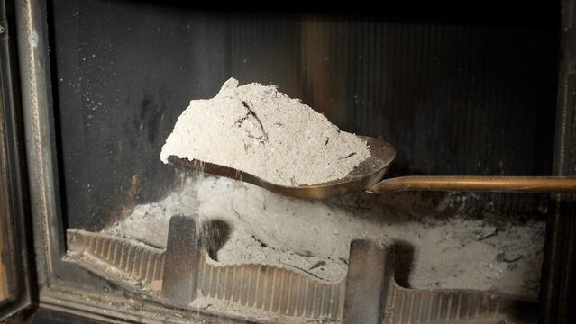 Cleaning a fireplace, scooping ash with a metal shovel inside a wood-burning stove