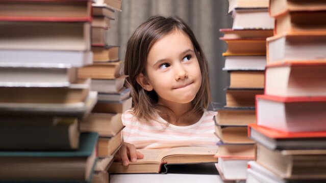 Young girl reading an open book surrounded by tall stacks of wisdom