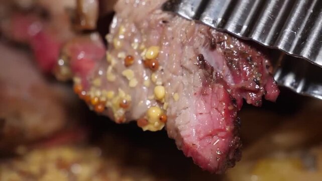 Close-up footage of juicy, sliced roasted meat, possibly corned beef or lamb, seasoned with a crust of whole mustard seeds and peppercorns. The shot highlights the tender texture and savory glaze of a