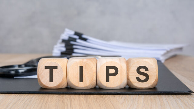 TIPS word on wooden blocks. Blurred background with a document stack and magnifying glass. Business advice and consulting concept.