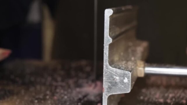 A close-up shot of a professional butcher wearing protective gloves using an electric industrial band saw to precisely cut through a large section of raw beef ribs and bone. The footage showcases the 