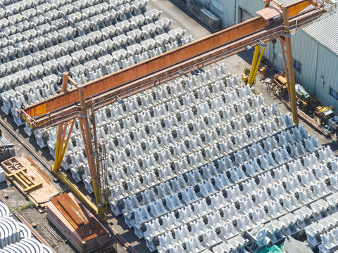 Aerial view of rows of concrete tetrapods stacked in an industrial yard with large orange gantry cranes under bright sunlight in Taiwan.