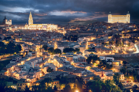 The ancient city of Toledo, Spain, at twilight with the illuminated Cathedral and Alcazar against a moody, dark sky.