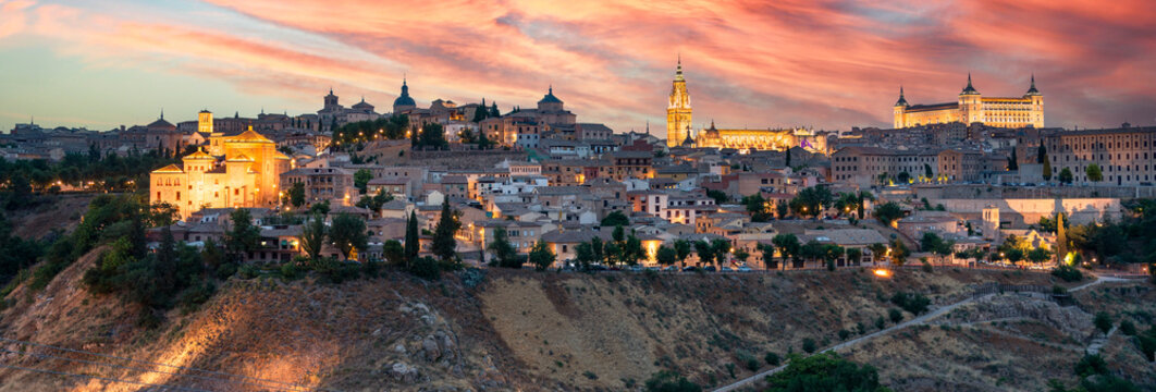 Panoramic shot captures the historic skyline of Toledo, Spain, at sunset, where the golden glow of the sky illuminates iconic landmarks like the Alc&aacute;zar and the Primate Cathedral.