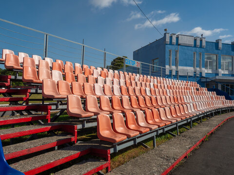 Detailed view of tiered rows featuring weathered blue plastic spectator chairs with rectangular recessed nameplate areas arranged on metal bleacher frames at a sports stadium or public venue.