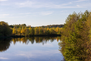 Obraz premium autumn lake in sunny weather at sunset, beautiful deciduous trees on the riverbank before the fall of leaves, evening before sunset