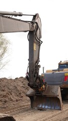 Precyzyjne roboty ziemne koparką gąsienicową: zbliżenie na łyżkę i ramię maszyny budowlanej podczas niwelacji terenu na profesjonalnym placu budowy © tomo81