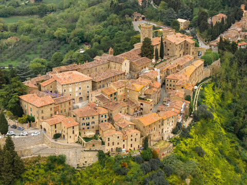 Aerial view of the medieval hilltop village with its historic stone buildings, terracotta roofs, and defensive tower surrounded by lush green hills in Parrano, Umbria, Italy.