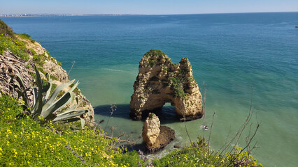 Natural rock arch formation surrounded by turquoise ocean water and coastal vegetation in the foreground. Scenic seaside landscape ideal for travel, summer and nature themed content. © TianaTi