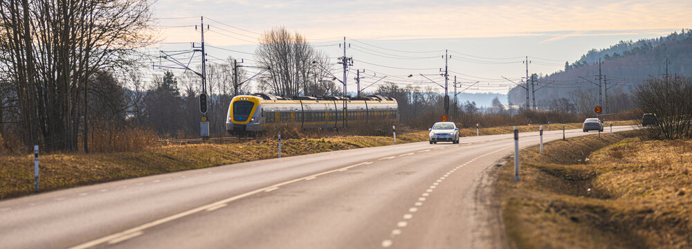 Kungsbacka, Sweden - March 20 2026: Rural road with passing car and modern train in countryside landscape at early spring daylight.