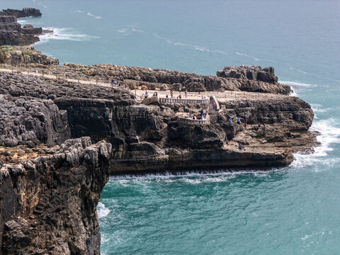 Aerial view of the rugged limestone cliffs of Boca do Inferno with tourists on the viewing platform overlooking the turquoise Atlantic Ocean, Cascais, Lisboa, Portugal.