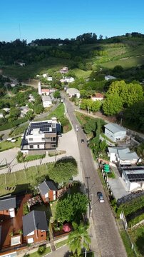 Vis&atilde;o a&eacute;rea de paisagem rural em Bento Gon&ccedil;alves, RS, com casas, &aacute;reas verdes, vinhedos, estrada sinuosa e propriedades entre colinas da Serra Ga&uacute;cha.