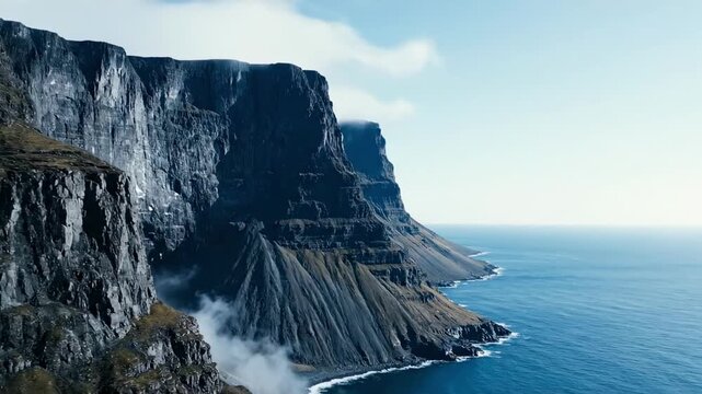 Steel gray mountains meeting the ocean along a remote cliff bound coast, drifting sea fog and steep rock buttresses revealing a rugged northern shoreline of austere beauty and open water calm