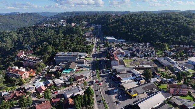 Vista a&eacute;rea de avenida central em Gramado com fluxo de ve&iacute;culos, constru&ccedil;&otilde;es t&iacute;picas e urbaniza&ccedil;&atilde;o destacando turismo e organiza&ccedil;&atilde;o da cidade