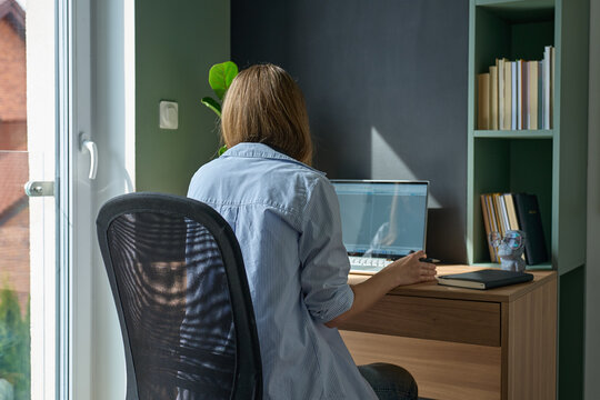 Woman sitting at desk and using laptop in home office near window