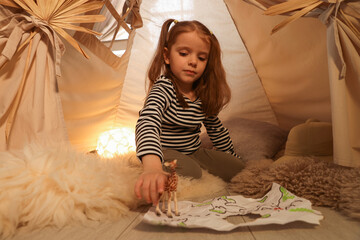 Little girl with drawing of map and toy giraffe near wigwam at home © New Africa