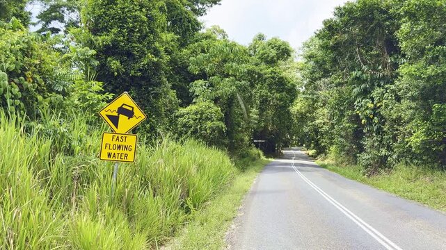Yellow and black flood warning road sign showing a car in water in the Daintree Rainforest near Cape Tribulation, North Queensland, Australia. Tropical hazard and travel safety concept.
