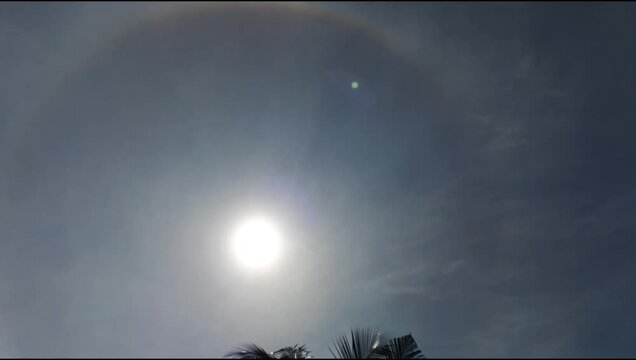 Sun halo phenomenon forming a circular rainbow ring around the sun in blue sky, rare natural optical atmospheric event.